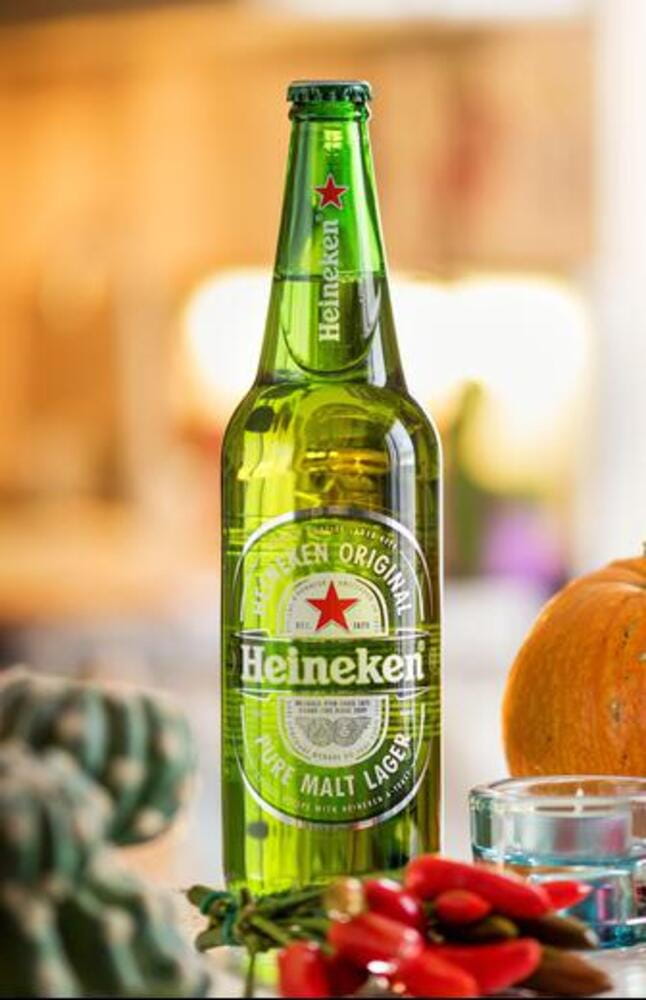 Glass green bottle of Heineken beer placed on counter against blurred background Glass green bottle of Heineken beer placed on counter against blurred background
