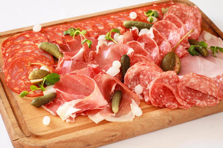Charcuterie board - A platter of ham & bacon slices with pickles on a wooden board Charcuterie board - A platter of ham & bacon slices with pickles on a wooden board