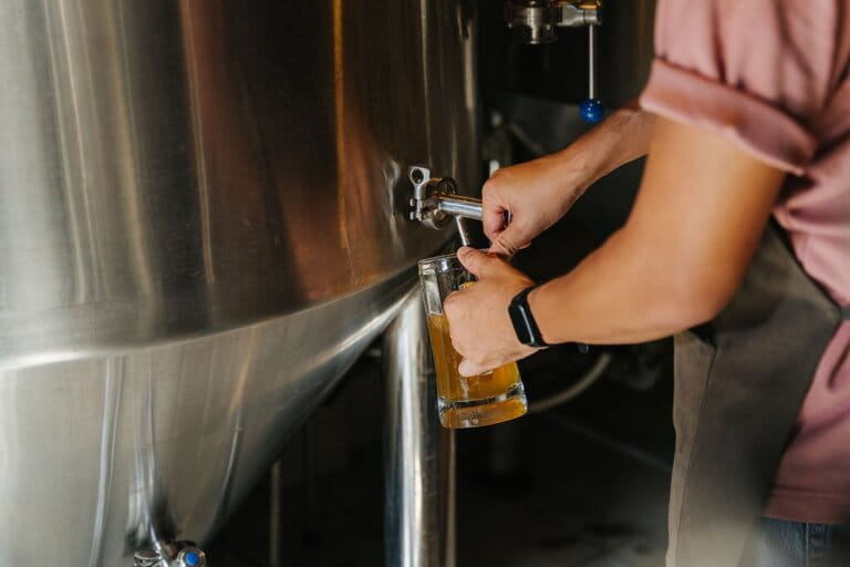 Brewer filling beer in glass from tank at brewery Brewer filling beer in glass from tank at brewery