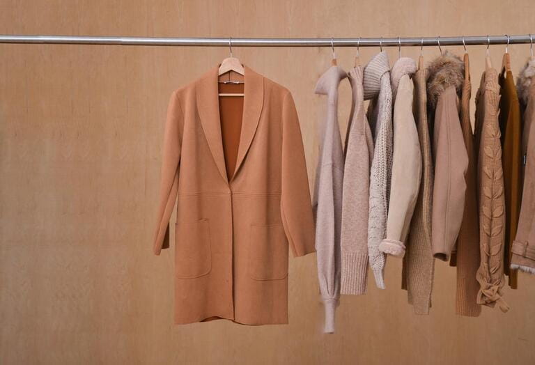 Row of different brown and warm knitted on hanger autumn, jacket, coat winter clothes-wooden background Row of different brown and warm knitted on hanger autumn, jacket, coat winter clothes-wooden background