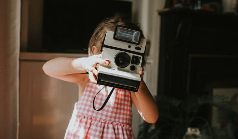 Young girl holding a vintage instant camera and taking a photograph. She presses the red shutter button and looks towards the camera.  Young girl holding a vintage instant camera and taking a photograph. She presses the red shutter button and looks towards the camera.