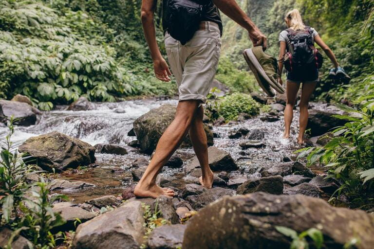 Shoot the low part of men and women crossing the stream barefoot. Couple walking by the creek in the woods with their shoes in hand. Hiking in the woods. Shoot the low part of men and women crossing the stream barefoot. Couple walking by the creek in the woods with their shoes in hand. Hiking in the woods.