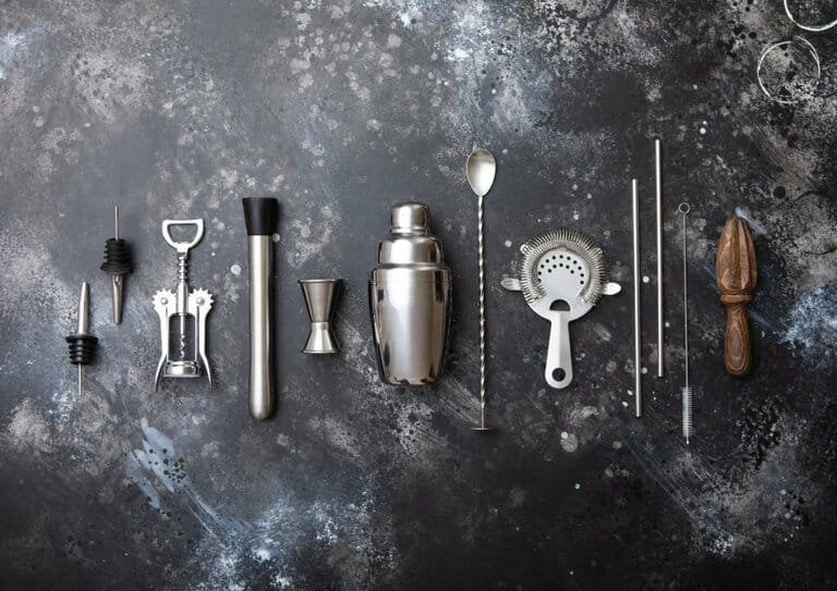 Black matte steel cocktail mixer on blackboard. Shaker, wine opener, spoon, strainer, muddler and jigger with wooden manual juicer. Black matte steel cocktail mixer on blackboard. Shaker, wine opener, spoon, strainer, muddler and jigger with wooden manual juicer.