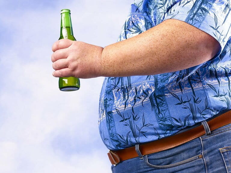 Obese man holding beer bottle against sky Obese man holding beer bottle against sky