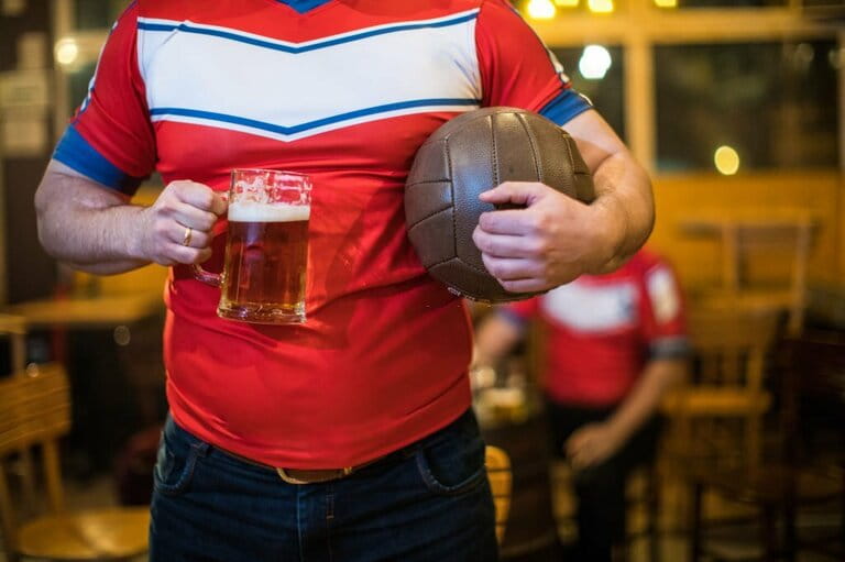 Man in sports uniform holding beer and ball in bar Man in sports uniform holding beer and ball in bar
