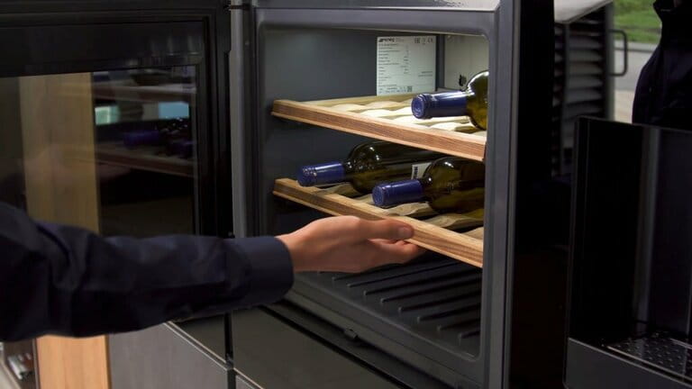 Wine bottles cooling on cold wooden shelves. Household appliances. Close-up of wine cooler used at home, man opening the cooler door Wine bottles cooling on cold wooden shelves. Household appliances. Close-up of wine cooler used at home, man opening the cooler door