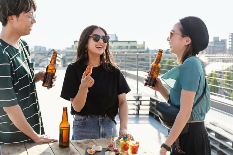 Young Japanese man and two women standing on a rooftop in an urban setting, drinking beer. Young Japanese man and two women standing on a rooftop in an urban setting, drinking beer.
