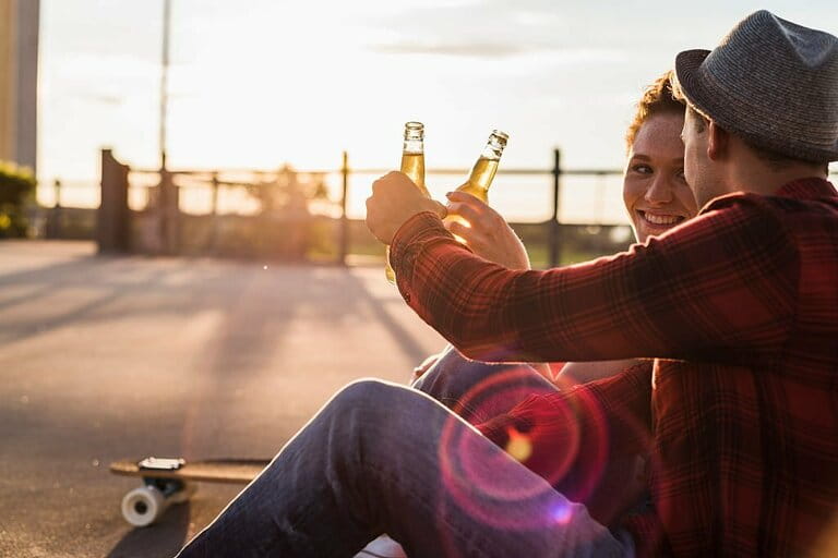 Young couple clinking beer bottles at sunset  Young couple clinking beer bottles at sunset